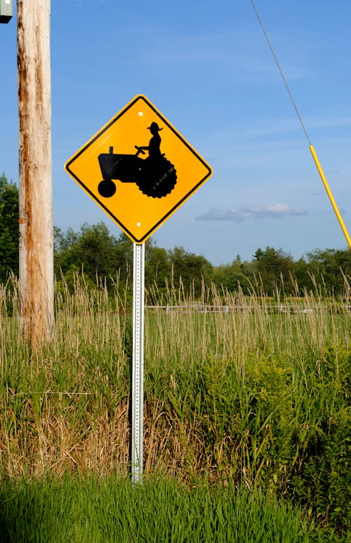 Warning yellow road sign with tractor placed on roadside in lush grassy countryside