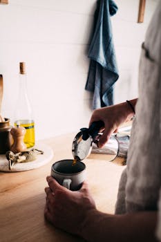 Person pouring fresh coffee into a mug on a wooden kitchen counter for a cozy morning start.