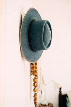 A chic blue hat elegantly hangs on a wall, complemented by decorative beads.