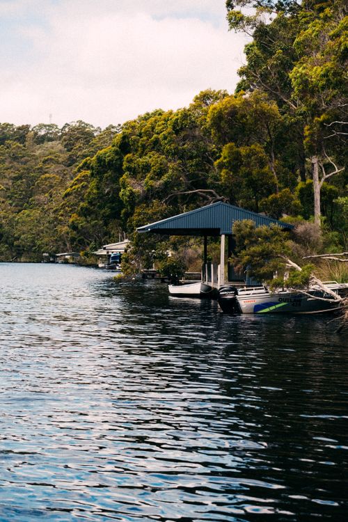 Free A peaceful riverside scene with motorboats docked beside lush green trees. Stock Photo