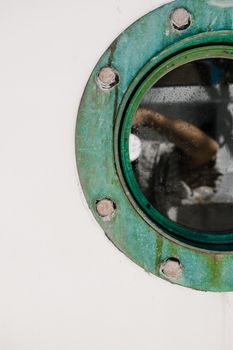 Detailed view through a rustic green ship porthole with water droplets.