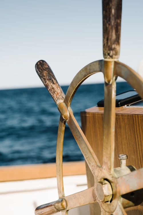 Free Close-up view of a vintage ship's wheel with a scenic ocean backdrop, showcasing nautical charm. Stock Photo
