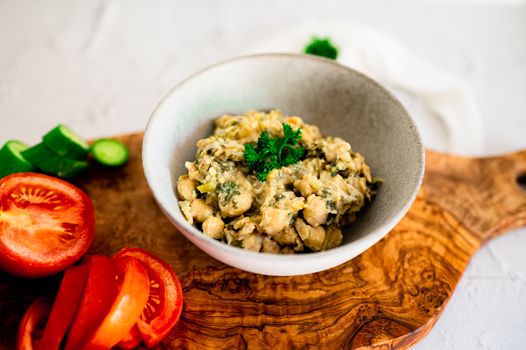 A delicious bowl of chickpeas with herbs and fresh tomatoes on a wooden board.