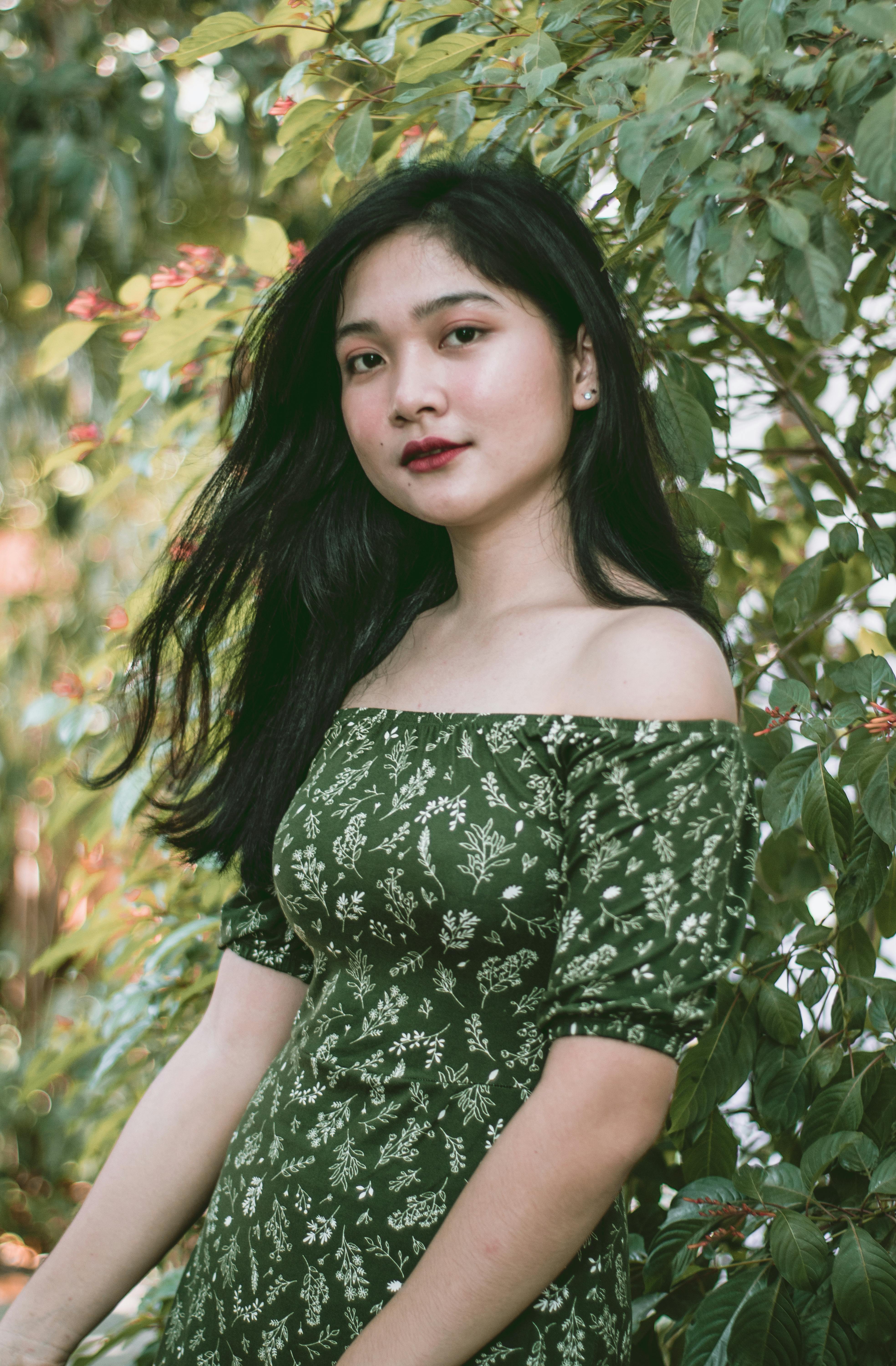 Portrait of a woman in a green floral dress surrounded by lush leaves, capturing natural beauty.