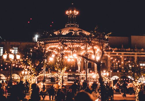Lively nighttime urban scene with lights and people celebrating at a city plaza.