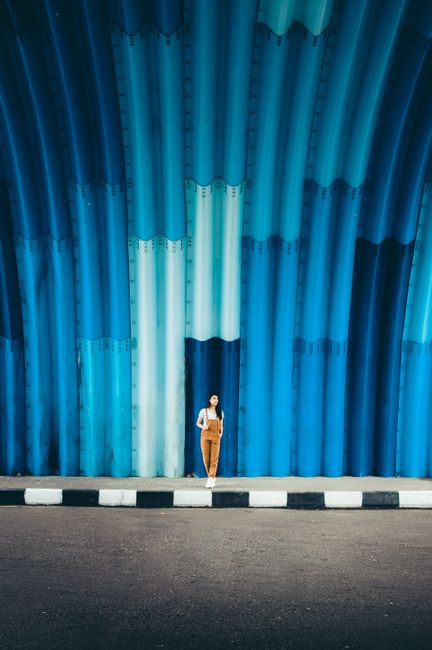 Young female in overalls standing on sidewalk of road against blue round shaped wall of tunnel