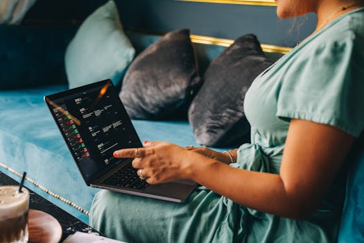 A woman in a green dress works on a laptop while seated on a sofa, illustrating remote work.