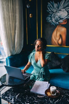 Woman in a green dress working on a laptop in a stylish interior with art decor.
