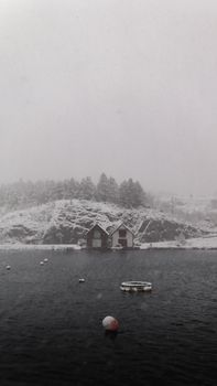Serene snowy landscape of waterfront houses in Vestland, Norway during a winter snowfall.