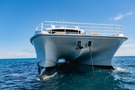 A close-up of a sleek luxury catamaran anchored on a calm ocean under a clear blue sky.