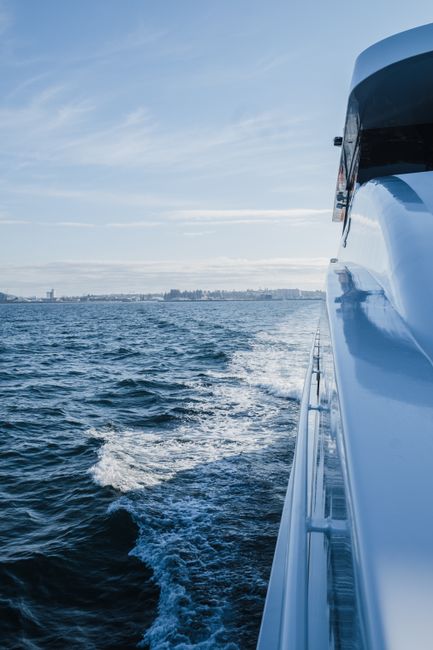 A luxurious yacht sailing through open blue ocean with a city skyline in the distance.