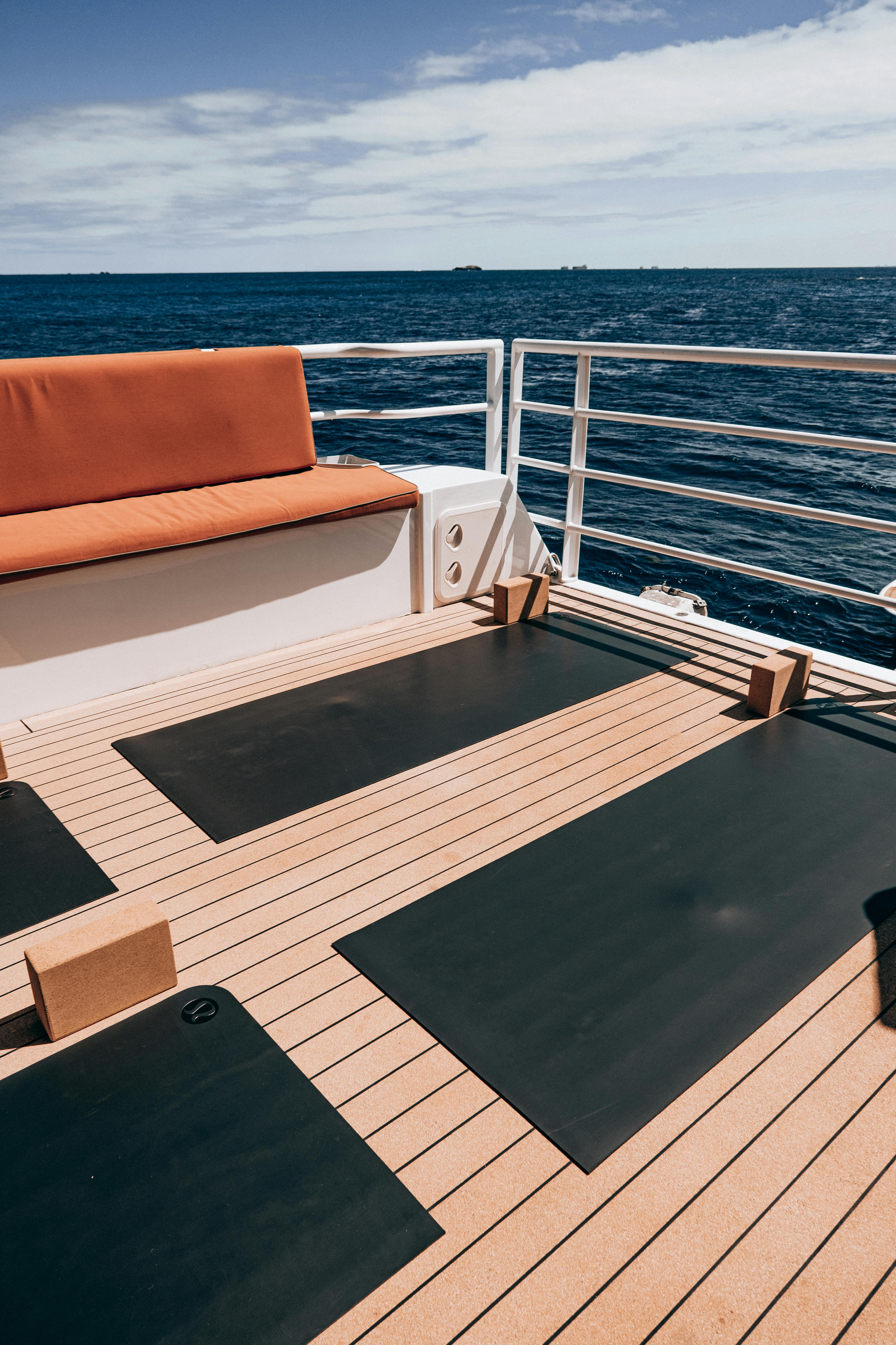 Sunlit luxury yacht deck featuring yoga mats and seating, overlooking the ocean.