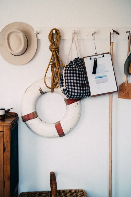 Free Nautical themed wall decor featuring lifebuoy, plaid bag, hat, and rope on white wall. Stock Photo