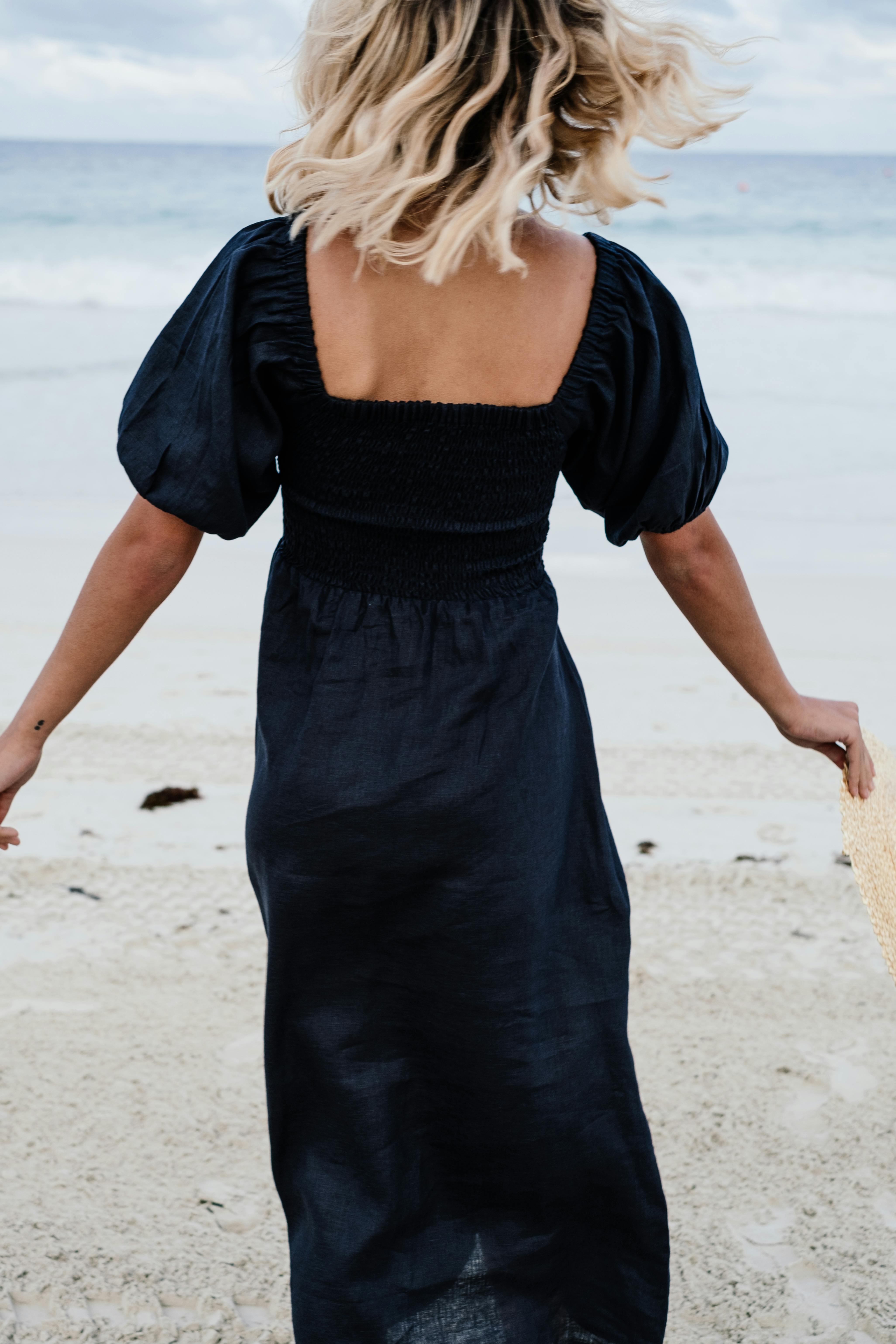 A woman in a black dress at the beach, enjoying the scenic ocean view.