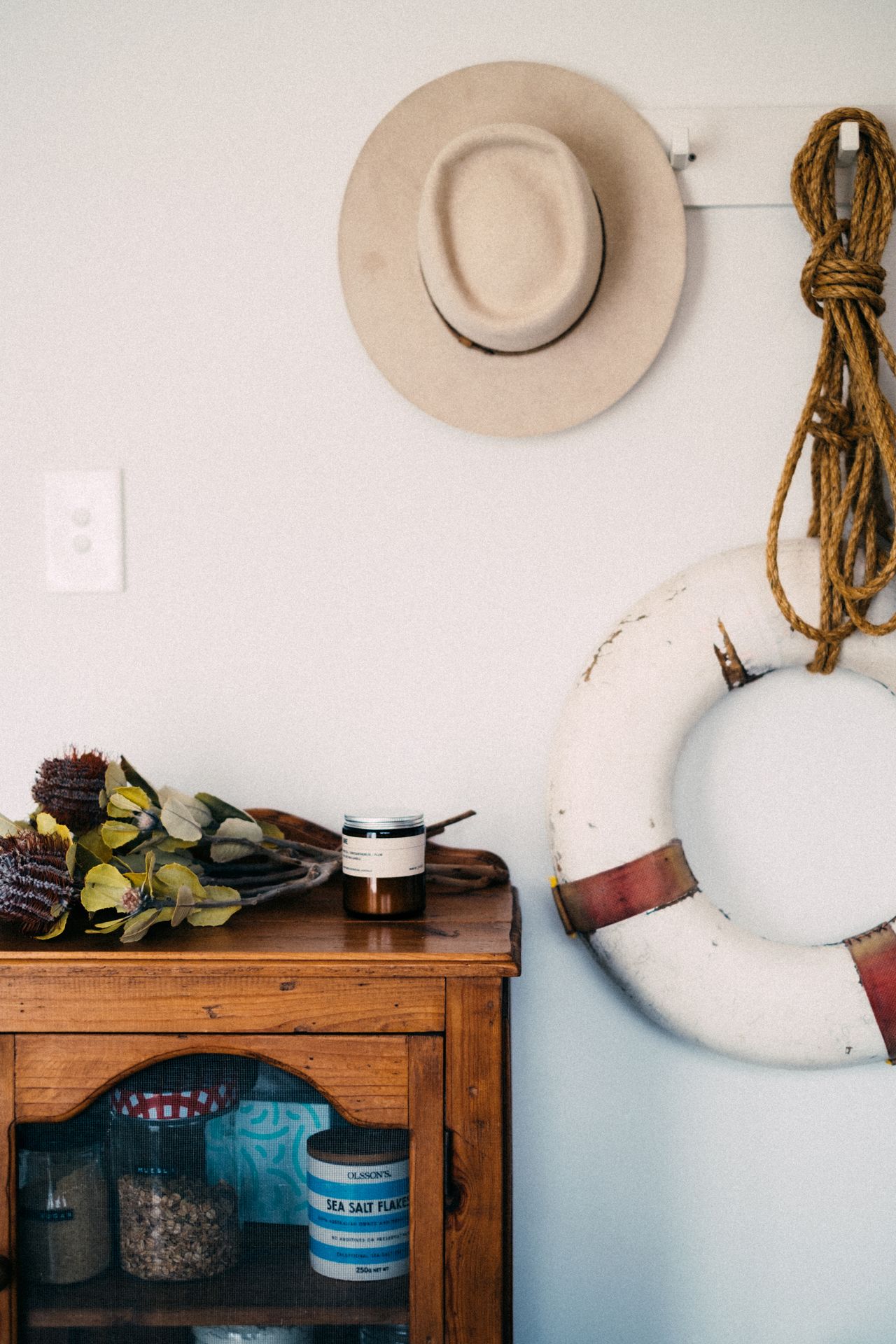 Nautical wall decor with a straw hat, coiled rope, and a vintage life ring above a wooden cabinet