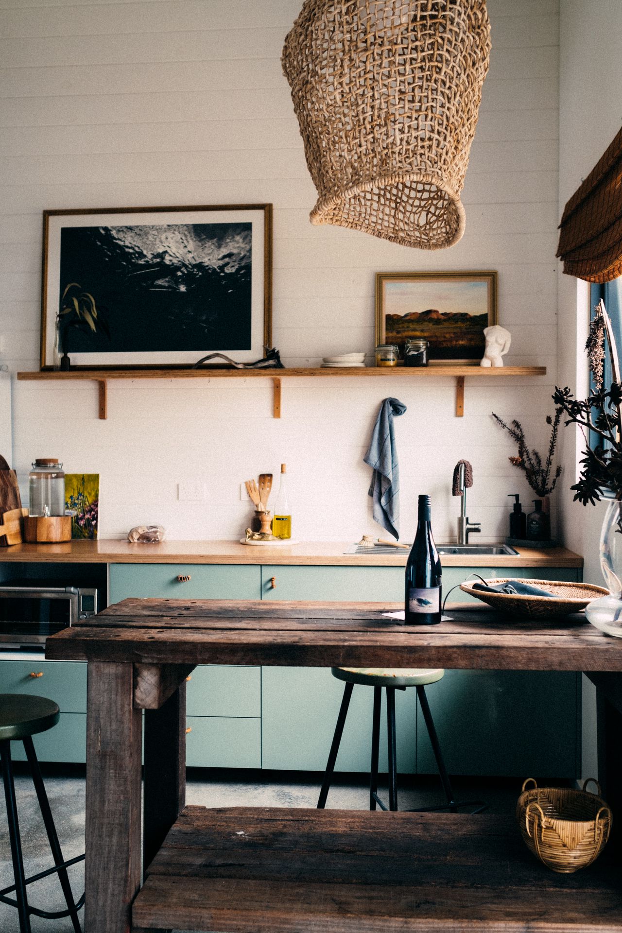 Small rustic kitchen with a chunky wood worktable, sage cabinets, and a woven pendant