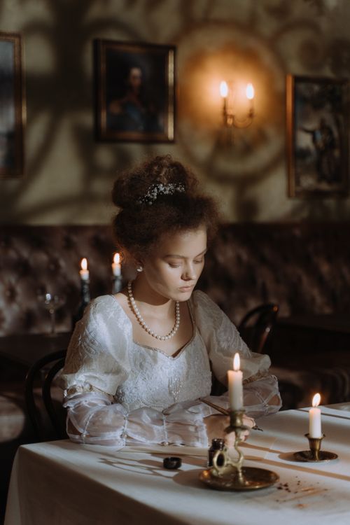 Free An elegantly dressed noblewoman writing by candlelight in a vintage setting, evoking historical aristocratic themes. Stock Photo