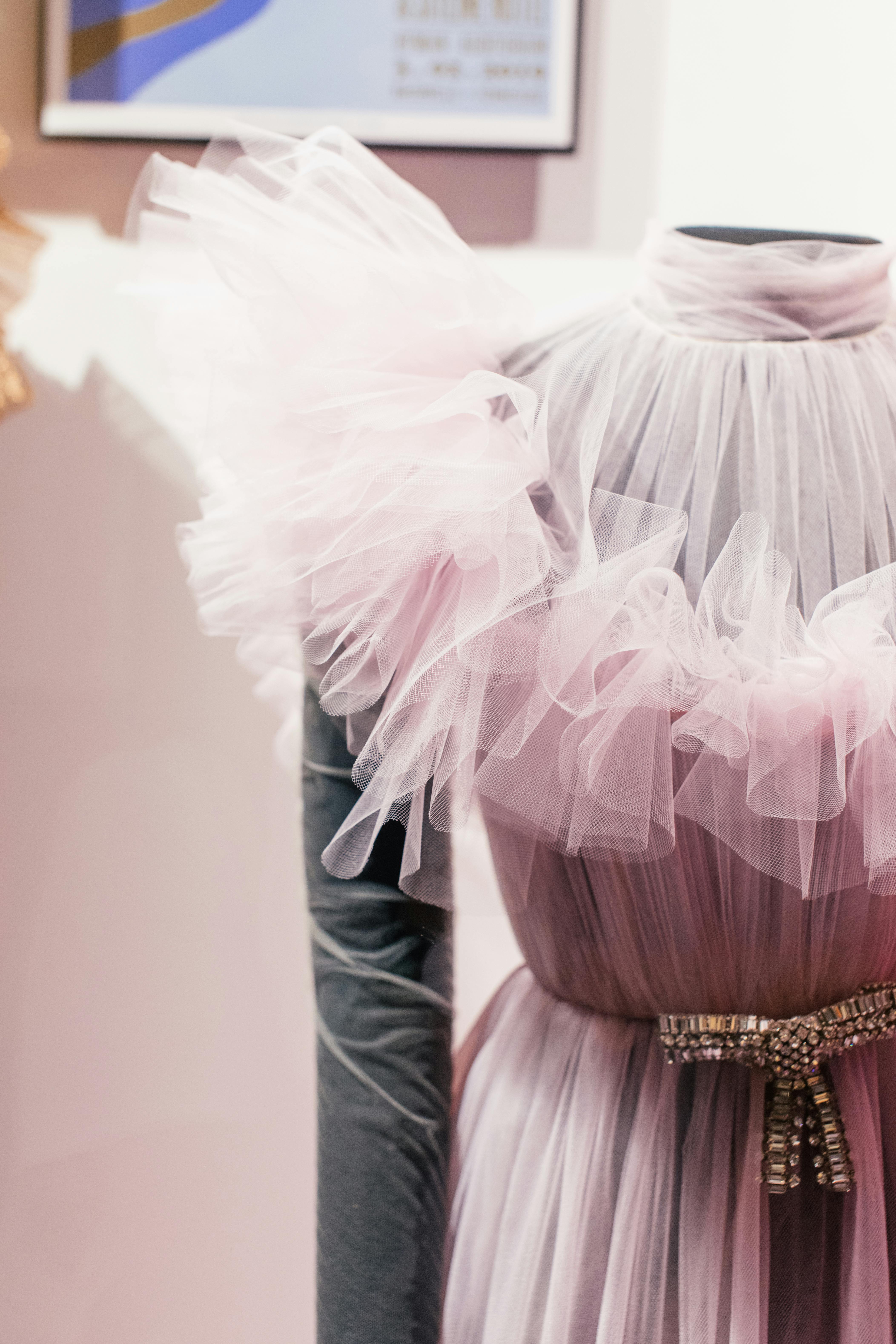 A stylish pink sheer gown with ruffled fabric showcased in a fashion studio, highlighting elegance and design.