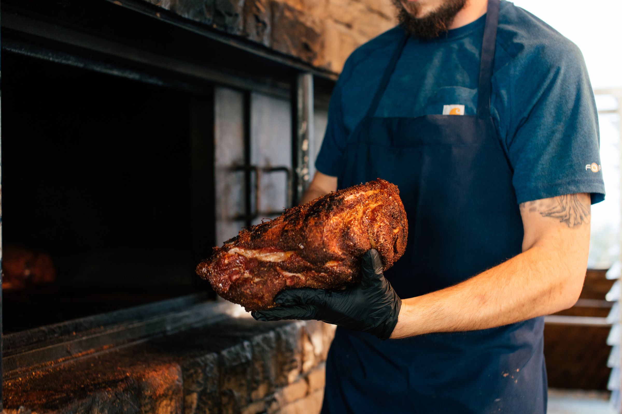 Chef holding smoked meat beside a barbecue pit