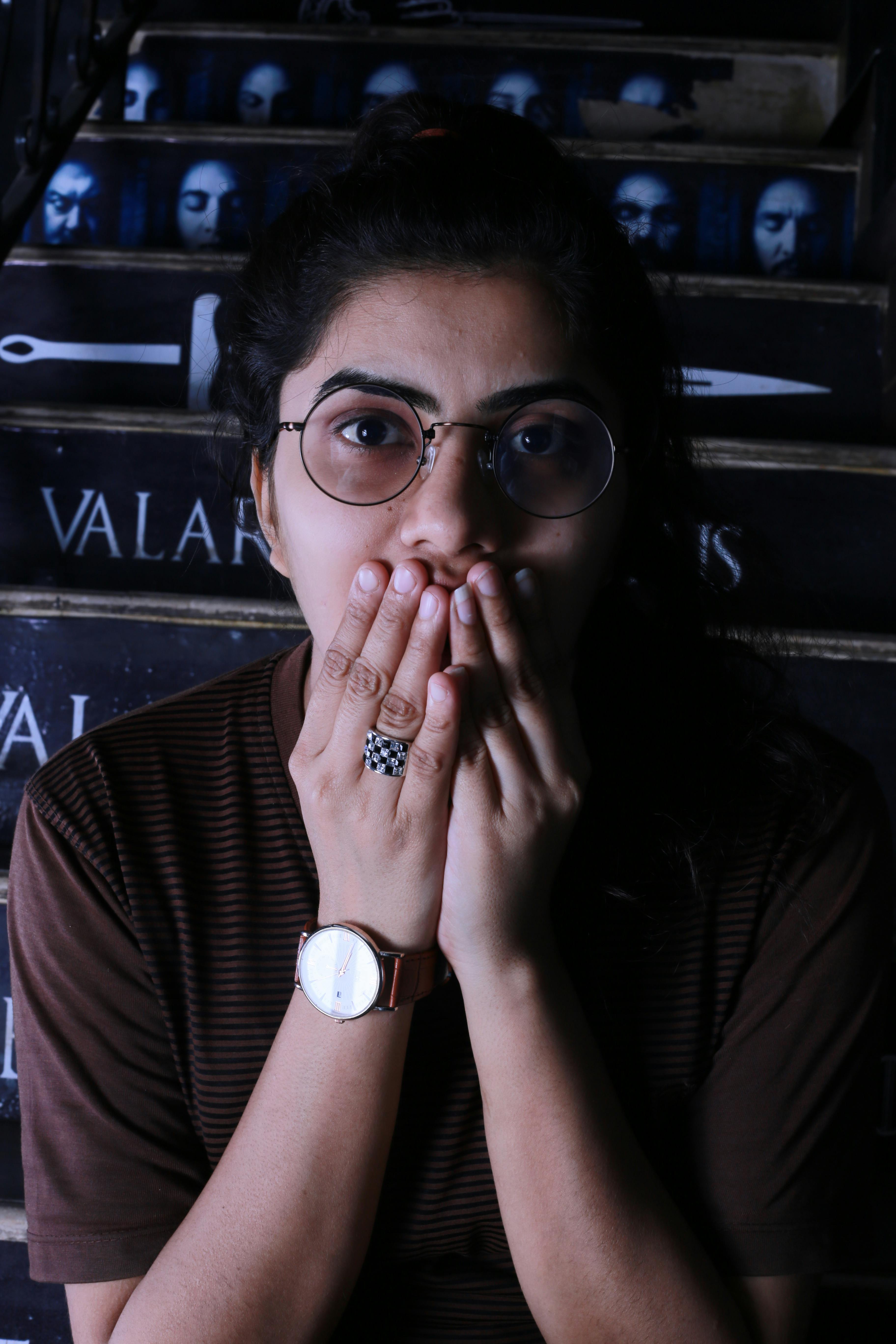 A surprised woman covers her mouth with her hands in a dramatic indoor portrait.