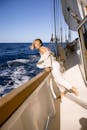 一名妇女斜靠在帆船的栏杆上，在开阔的水面上享受阳光明媚的一天