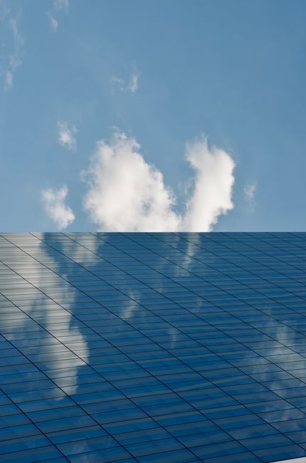 A glass skyscraper reflects clouds and blue sky, creating a modern architectural view.