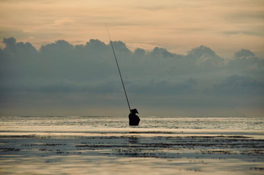 A lone fisherman in silhouette against a tranquil sunrise over Bali's waters, creating a serene and peaceful scene.