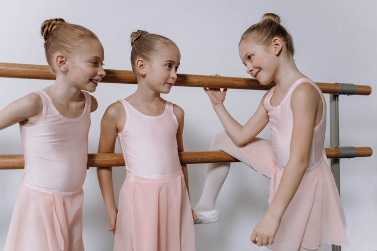 Girls In Pink Dress Leaning On A Ballet Barre While Having A Conversation