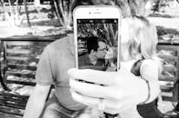 一对情侣在公园长凳上用智能手机自拍接吻