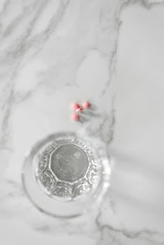 Close-up view of a glass of water and pink pills on a marble surface, representing medication concept.