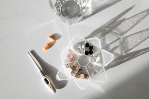 Free A detailed image showcasing a pill organizer, digital thermometer, and pills with a glass of water on a white surface. Stock Photo