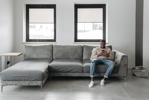 Cozy living room featuring a man on a sofa, using his smartphone for relaxed browsing.