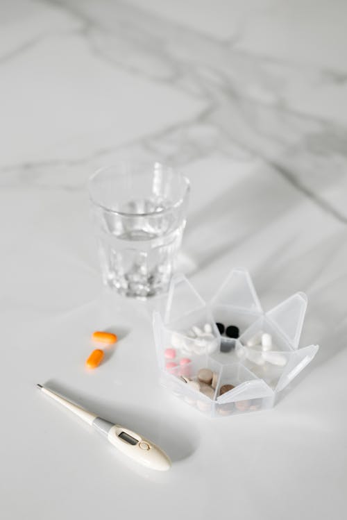 Medication Beside A Glass Of Water And Thermometer