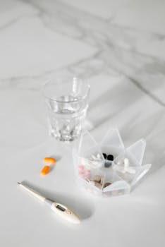 Organized medication, water, and thermometer on a white surface for daily health routine.
