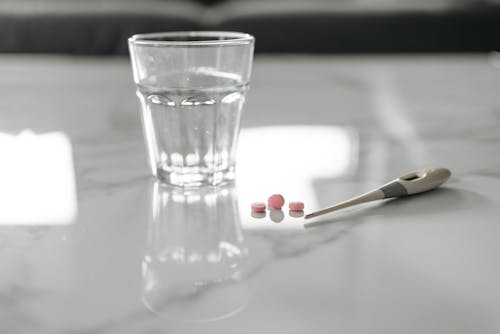Thermometer And Medicine Beside A Glass Of Water