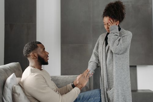 Free Man comforting woman with headache while sitting on a sofa indoors. Warm and supportive interaction. Stock Photo