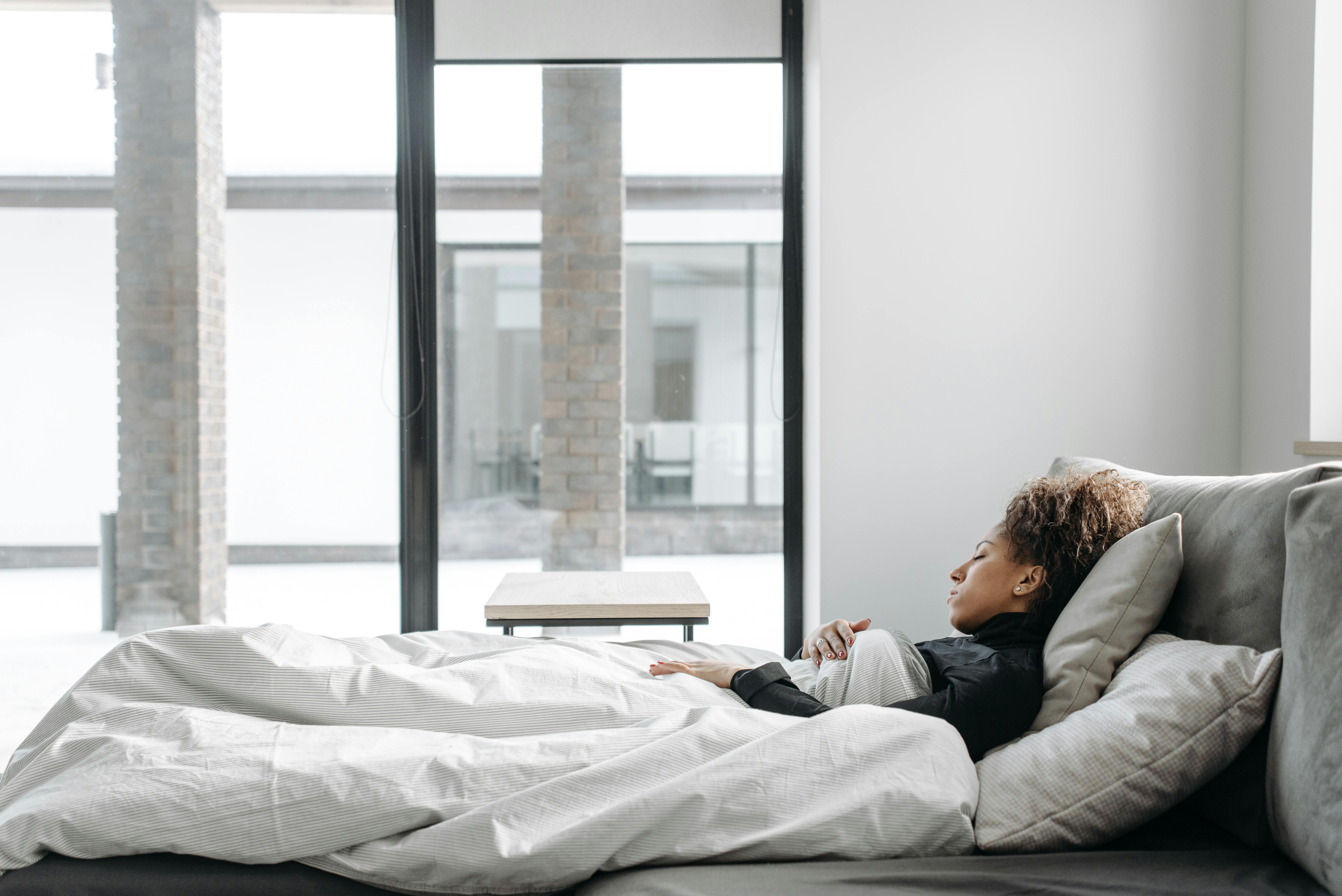 A woman rests comfortably in bed in a bright, minimalistic room.