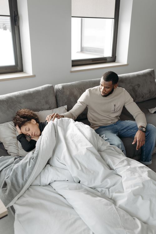 Free A caring man comforts a sick woman lying on a sofa in a cozy room, providing support. Stock Photo