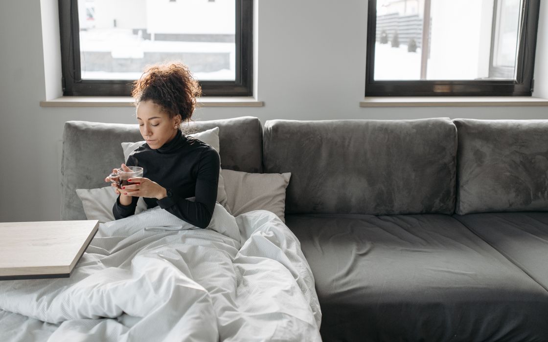 Young woman resting on a sofa under a blanket with a cup of tea at home