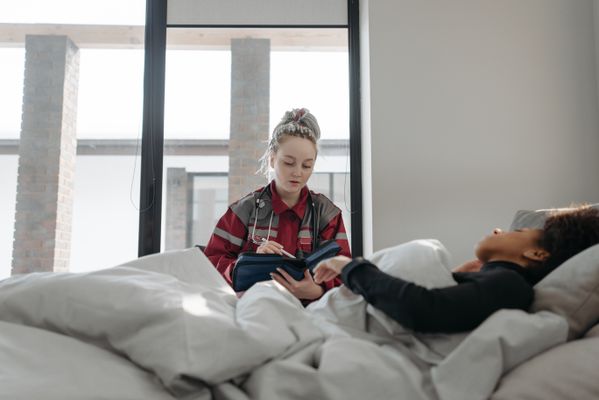 A healthcare worker takes notes while attending to a patient in bed, providing home healthcare