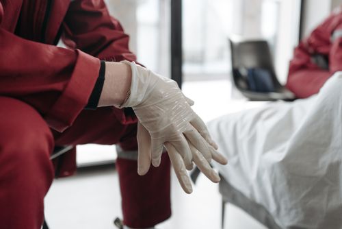 Free Healthcare worker in red uniform putting on latex gloves in a clinic setting. Stock Photo