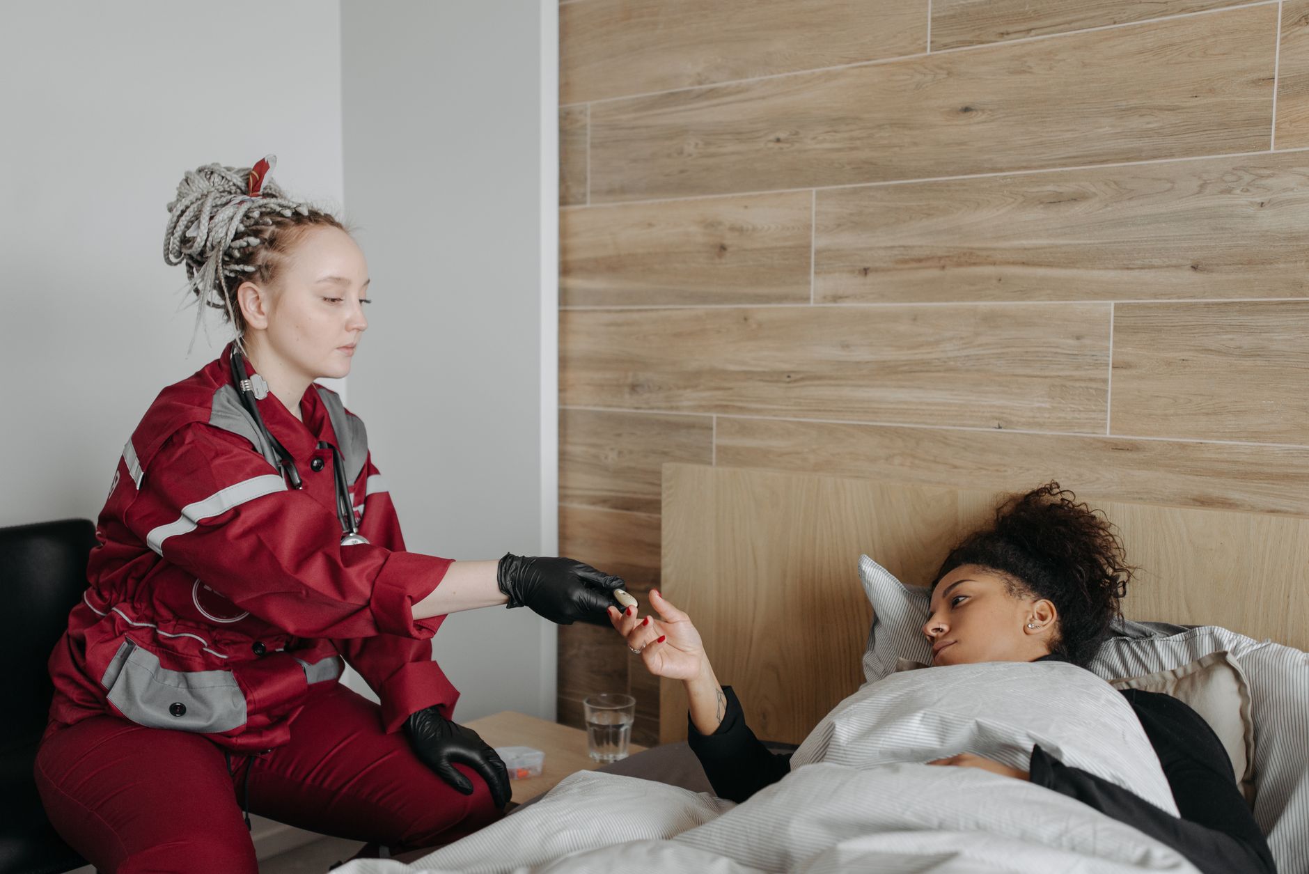 A paramedic provides care to a sick woman lying in bed, highlighting healthcare support at home.