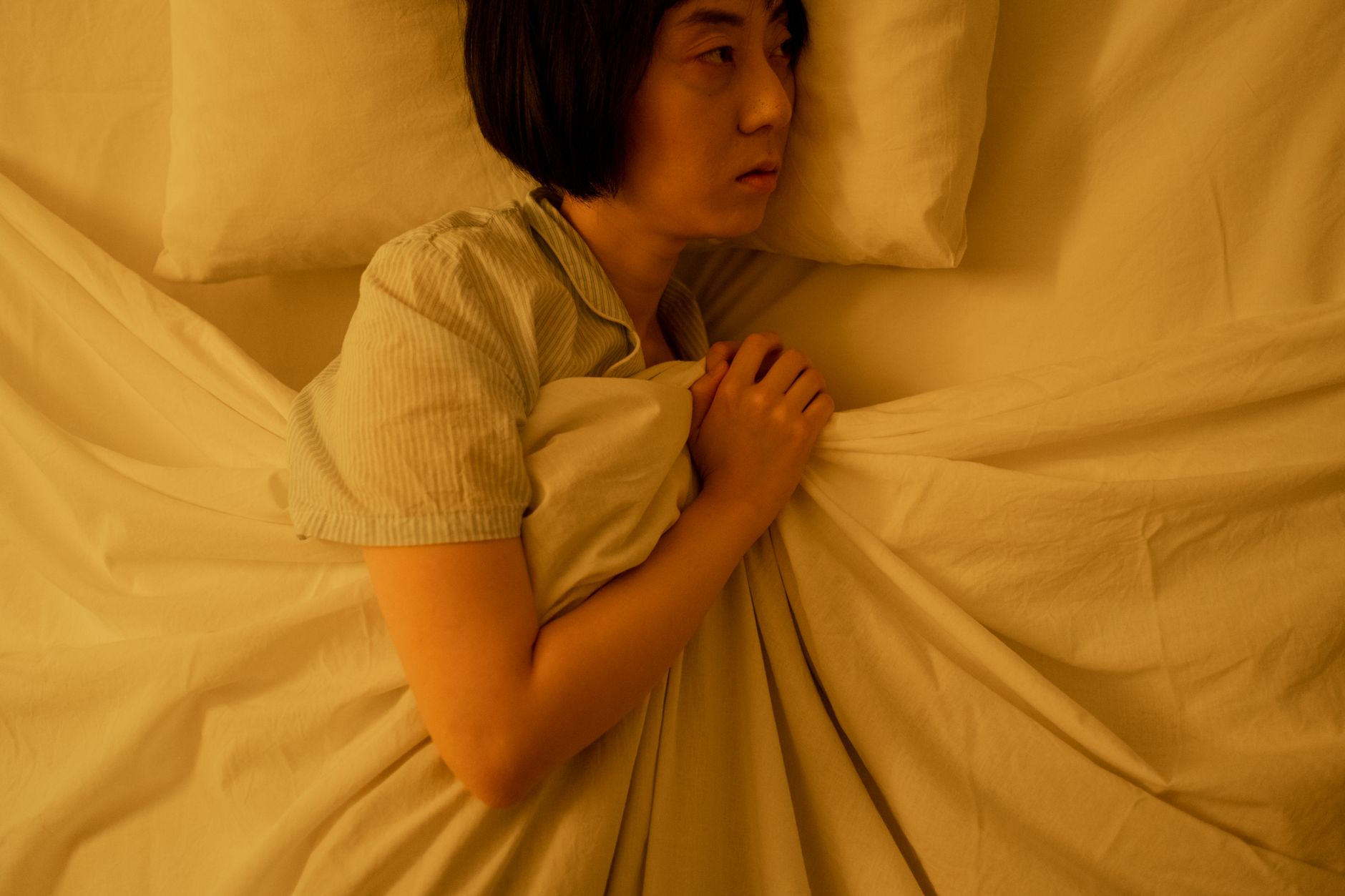 睡不著怎麼辦?中醫與西醫失眠差異全解析 Side view of an Asian woman lying in bed, reflecting anxiety and insomnia in dim light.