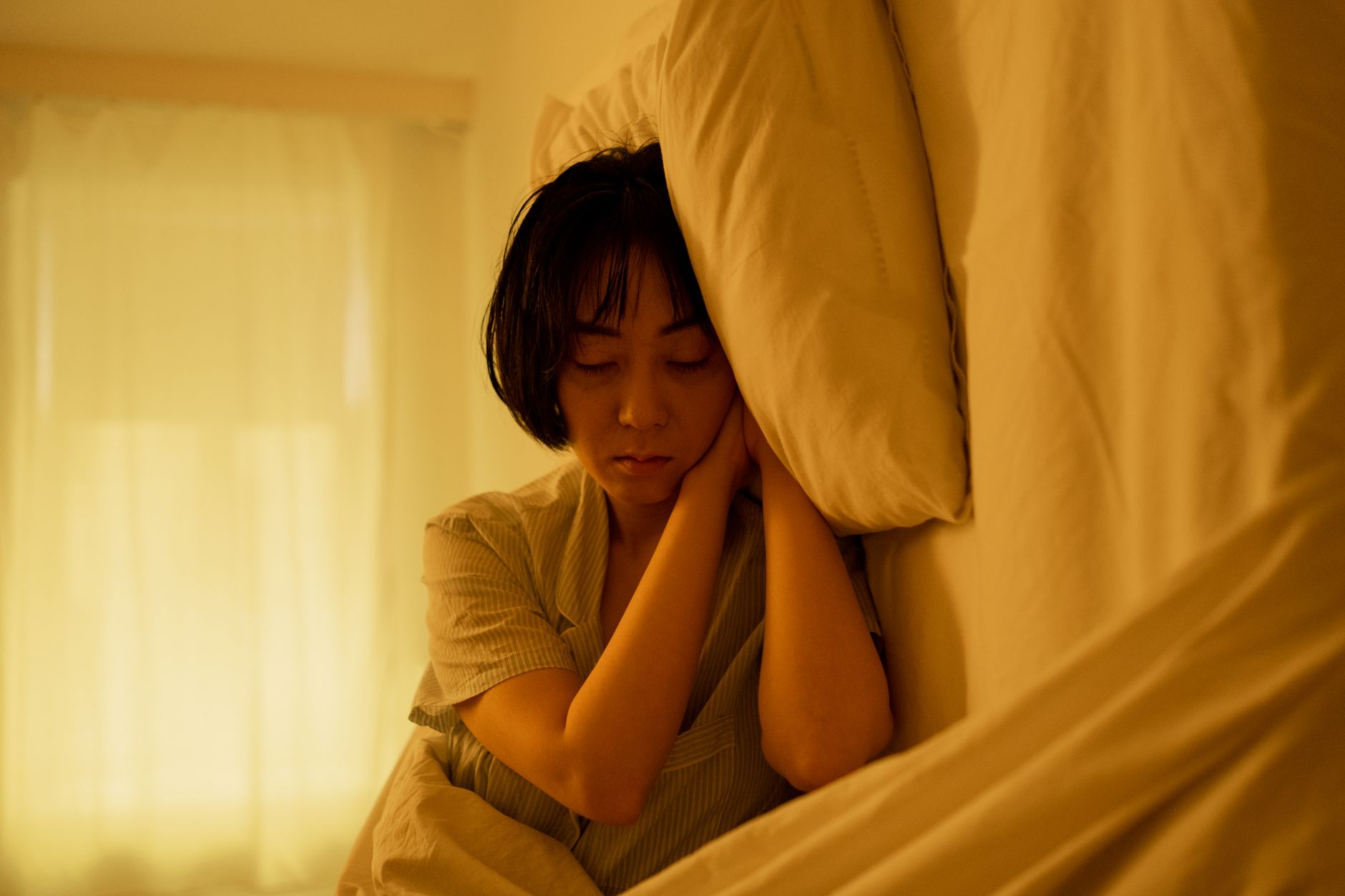 Asian woman resting peacefully in bed, conveying serenity and relaxation indoors.