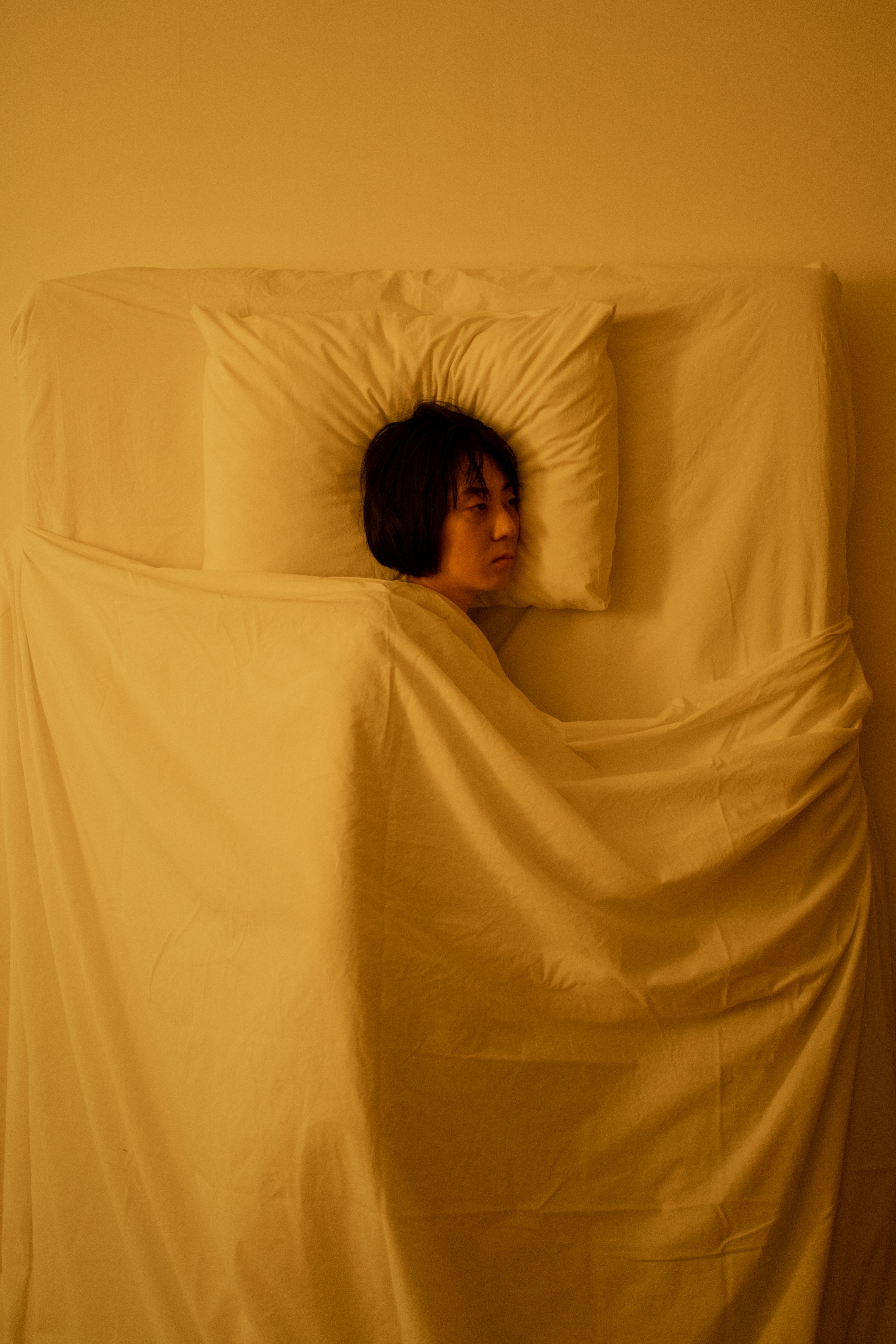 Asian woman lying in bed, lost in deep thought, portraying stress and exhaustion.