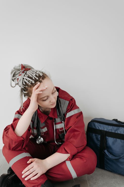 Free A tired female EMT in red uniform sitting on the floor, resting her head in her hand. Stock Photo