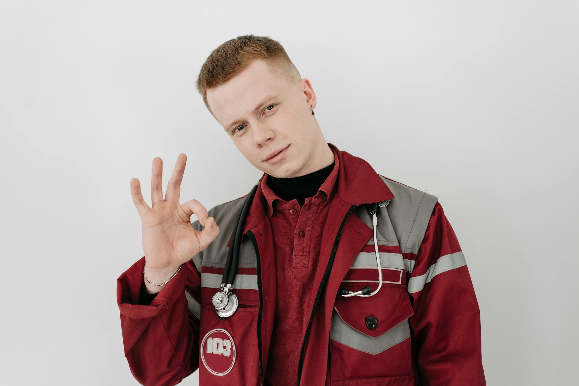 Male healthcare worker in medical uniform making an okay sign, conveying a friendly and reassuring demeanor.