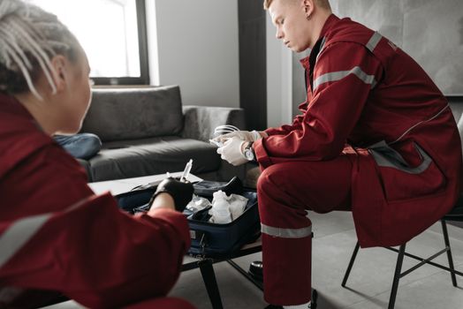 Paramedics in red uniforms attend to a medical emergency indoors, preparing medical equipment.