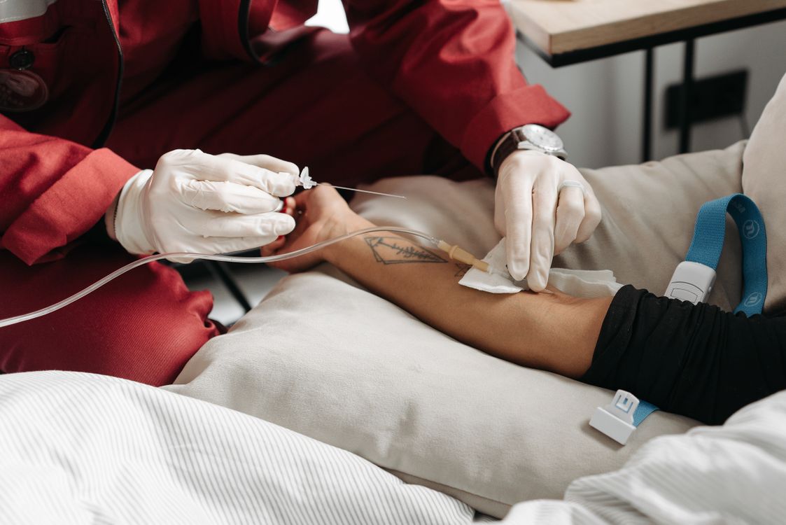 A nurse placing an IV line in a patient's arm during a mobile IV therapy session at their accommodation