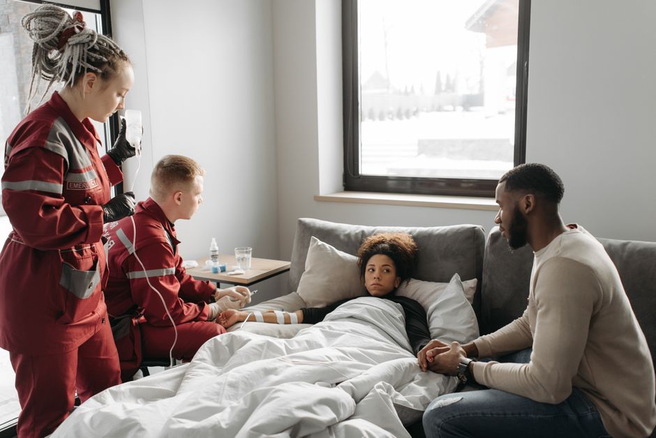 Paramedics provide care to a sick person at home, showcasing emergency medical assistance in a domestic setting.